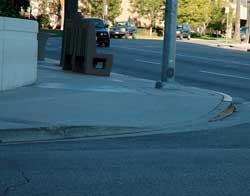 Очертание бортового камня на пешеходной дорожке. Слева на бетонном тротуаре видна профрезерованная ребристая полоса, позволяющая слепому палкой нащупать начало спуска к пешеходной дорожке.